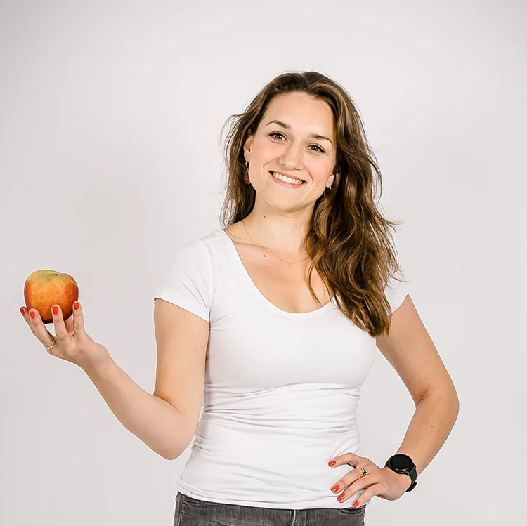 Die Ernährungstherapeutin Paulina von Wieding lächelt und hält einen roten Apfel in der Hand.