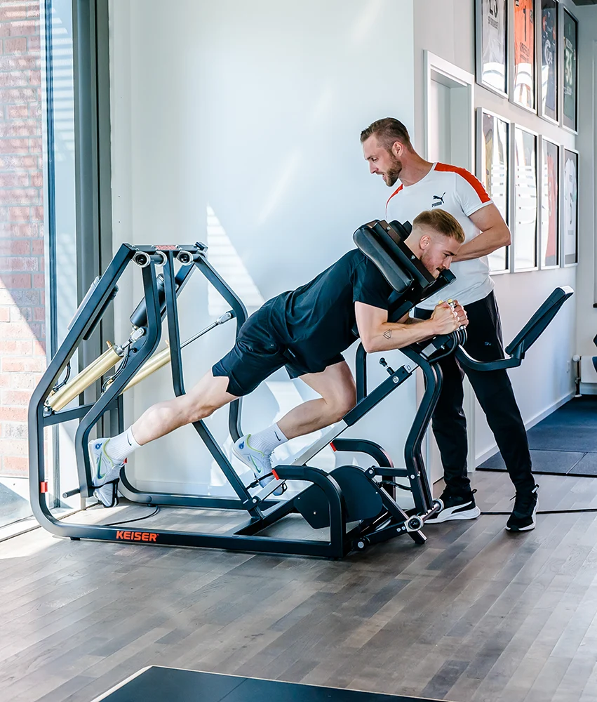 Der Sportwissenschaftlicher Patrick Reich trainiert einen Kunden in einem Sportgerät für Kraftausdauertraining.